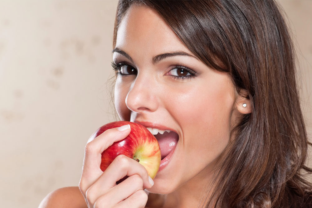 Smiling young woman eating apple | Oral health