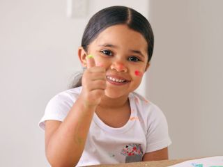 Smiling young girl with thumbs up fingerpainting
