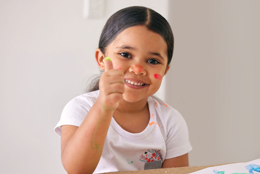 Smiling young girl with thumbs up fingerpainting